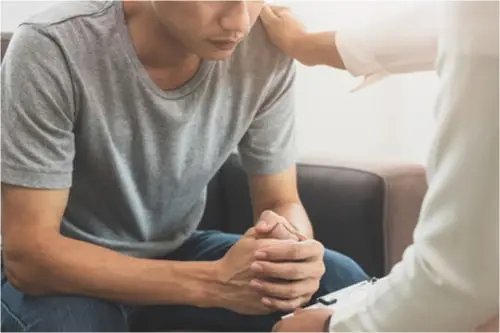 Close up of a sad person leaning & clutching hands with another person comforting them