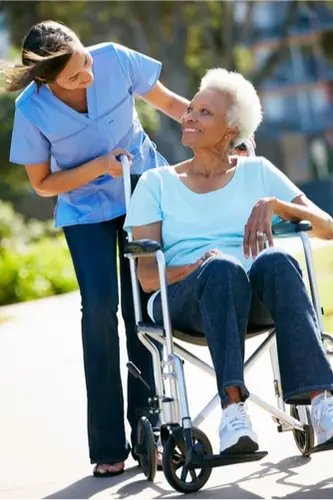 Caregiver pushing wheelchair with a woman in it in a park both are smiling