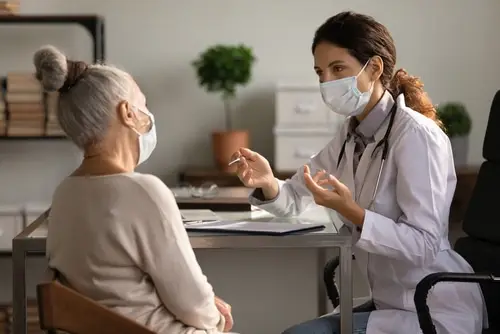 Doctor speaking to a mature woman in her office they both have masks on