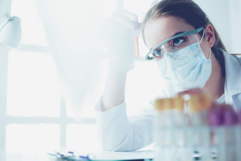 Female lab assistant holding up and looking at a test tube