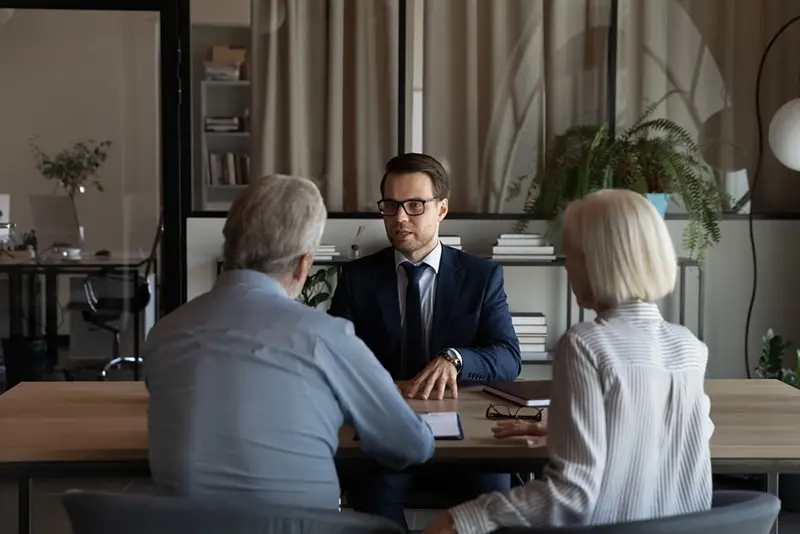 Mature couple at a man's desk in an office, he is speaking to them