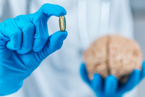 Hands in blue surgical gloves holding model of human brain and placebo pill