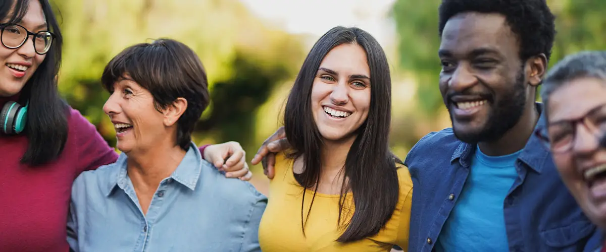 Group of happy people standing outside with their arms around each other's shoulders