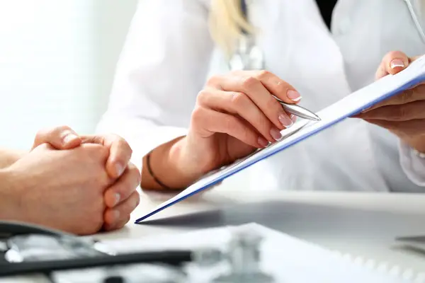 Doctor holding silver pen to a form showing the form to a patient