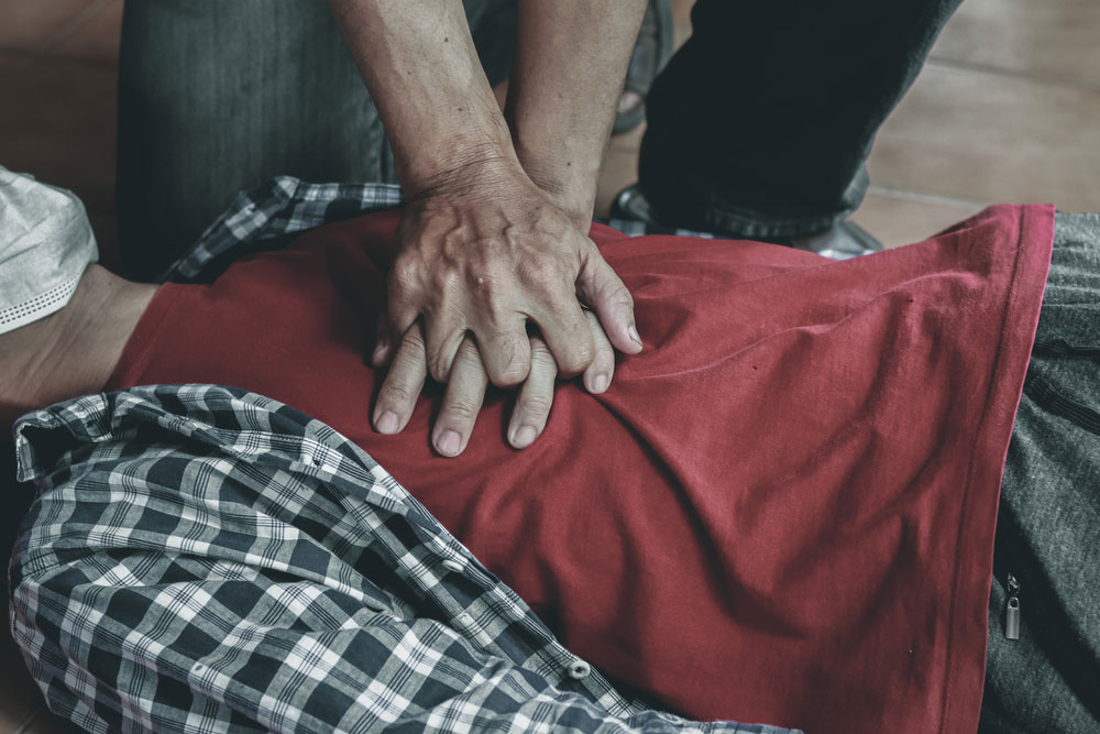 Close up of man's chest as he is laying on the ground while someone is performing CPR