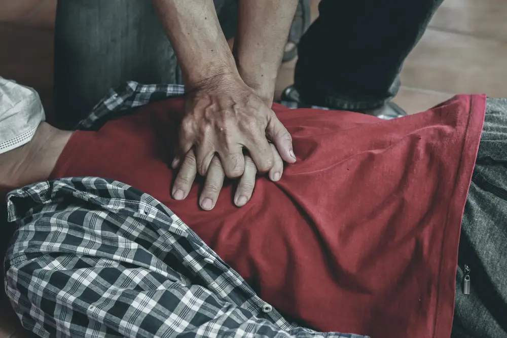 Close up of man's chest as he is laying on the ground while someone is performing CPR